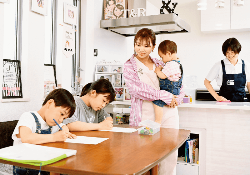 読者モデルの莉早ママが下の子を抱っこしながら子どもたち2人の宿題をみている画像
